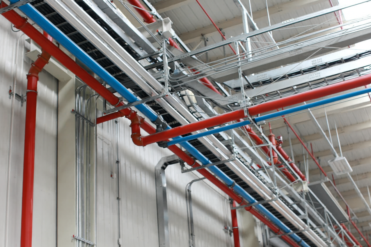 a network of pipe in different directions on the wall and connected to other pipe parallel to the ceiling made of different materials and of different colors